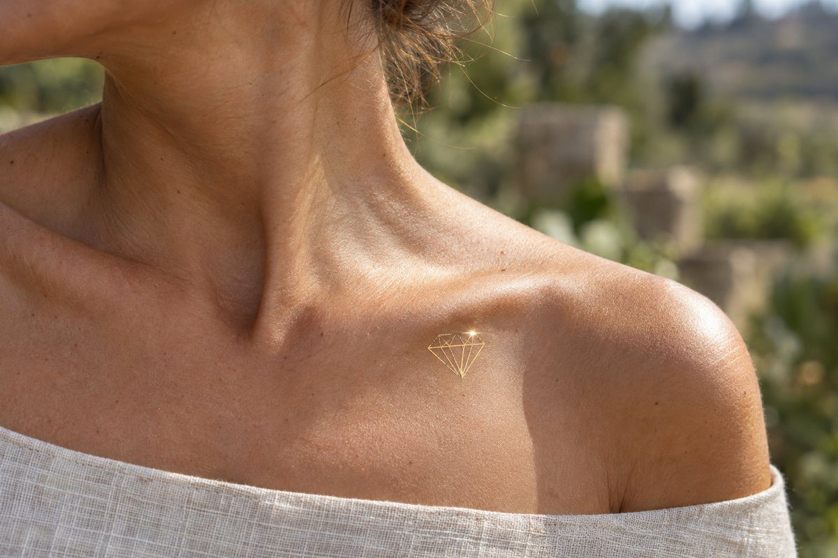 Tatouage diamant doré éphémère sur la clavicule accrochant le soleil d'été